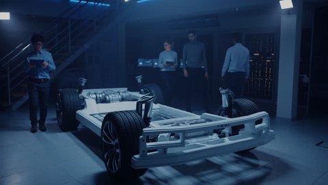 Automobile Engineers Working on Electric Car Platform Chassis Prototype, Using Tablet Computers with CAD Software for 3D Concept. In Automotive Innovation Facility Vehicle Frame with Wheels