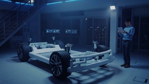 Automobile Engineer Working on Electric Car Chassis Platform, Using Tablet Computer Augmented Reality with 3D CAD Software Modelling. Innovative Facility: Vehicle Frame with Wheels, Engine, Battery