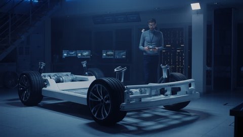Automobile Engineer Working on Electric Car Platform Chassis Prototype, Using Tablet Computer with 3D CAD Software Modelling. Innovative Facility: Vehicle Frame with Wheels, Engine,Battery. Shot on 8K