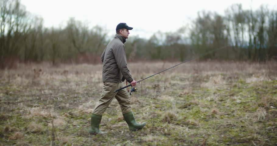Man Holding Fishing Rod Walking Amidst Bare Trees