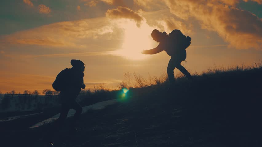Couple hiking help each other silhouette in mountains. Teamwork couple hiking, help each other, trust assistance, sunset. Man giving hand a woman to help her to climb the mountain. Royalty-Free Stock Footage #1026577676