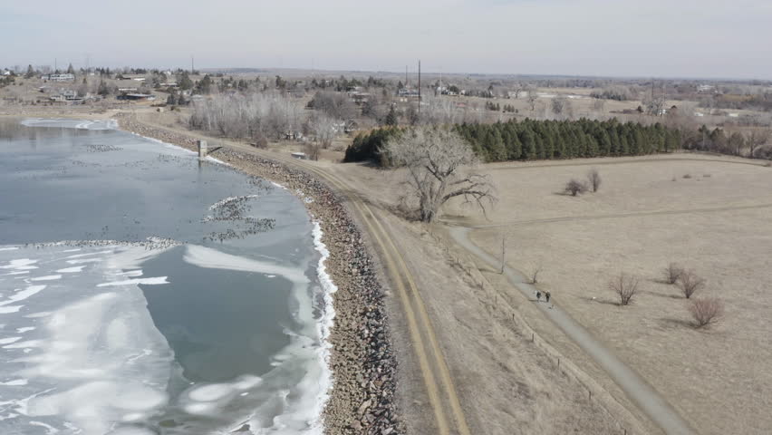 Two Active Senior Citizen Adults Walking Trail With Dogs Outdoors Along Frozen Lake Aerial Drone View Retirement Exercise
