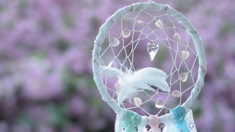 a spiritual symbol, a dream catcher with a diamond heart, on a pink background of a flowering shrub in the summer garden.