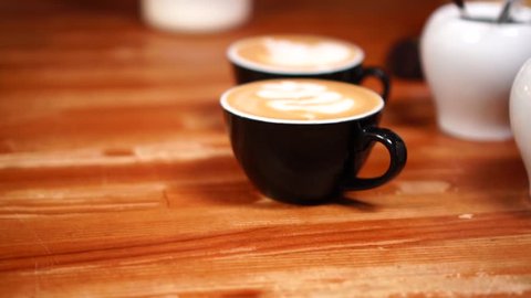 Close up view on small black minimalistic coffee cups with cappuccino and hot milk foam latte art in slow motion