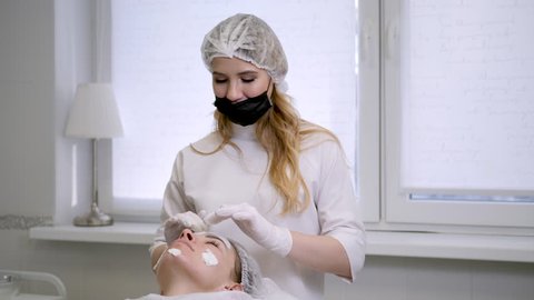 doctor cosmetologist in rubber gloves apply cream on the face of a young woman