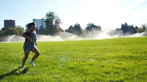 Girls tumbling and doing cartwheels in park by sprinklers