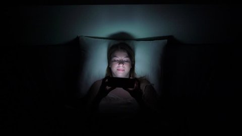 Young woman using mobile phone on the bed before she sleeping at night. Mobile addict or insomnia concept.