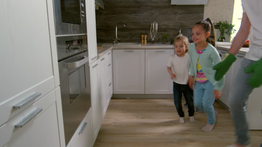 Two excited primary school girls and their father taking freshly baked pizza out of oven and putting it onto kitchen table