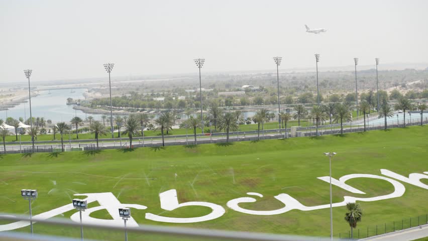 Abu Dabhi sign on the grass at Yas Marina Circuit in UAE with airplane flying on sky
