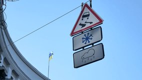 Road signs waving on wire under the street - slippery road when it is snowy or rainy weather. Ukrainian flag waving on background as concept of unstable political situation. View from the ground video