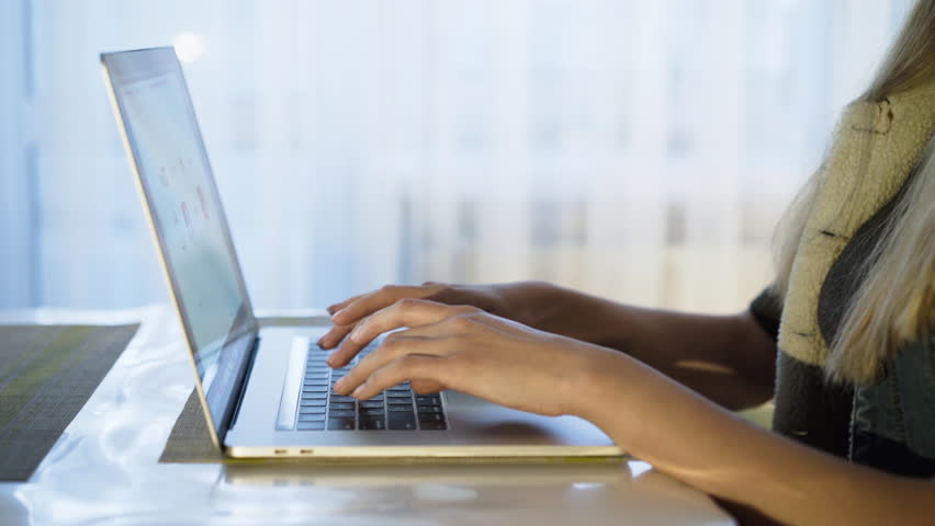 Female hands with right posture typing on laptop keyboard at window. Close-up. 4K