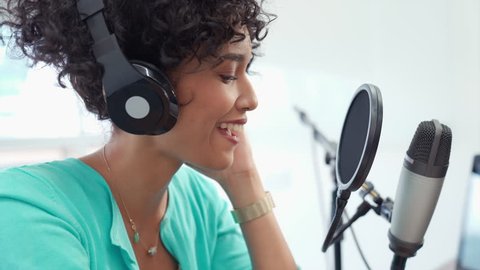 Good looking young black female recording a podcast recording for her online show. Attractive millennial African American business woman using headphones in front of microphone for radio program.