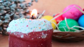 Seamless looped video close-up of burning candle made in the shape of easter cake. Basket with bright colored eggs and blooming willow branches with fluffy buds on background
