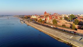 Torun old city in Poland. Aerial flyby video in sunrise light with medieval Gothic St John Cathedral, town hall tower, historic buildings, town walls, gates and Vistula river with 2 rowing boats
