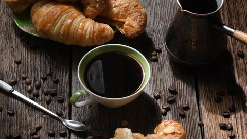 Coffee composition. Coffee Cup, croissants, coffee beans and copper coffee maker on old wooden table backgrounds. 4 K picture.