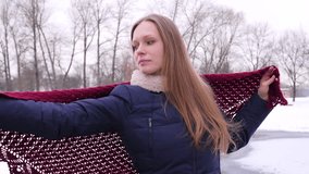 Portrait of a blue-eyed pretty smiling woman which puts shawls on her shoulders and looks into the camera in the winter city park in 4K slow motion close up video.