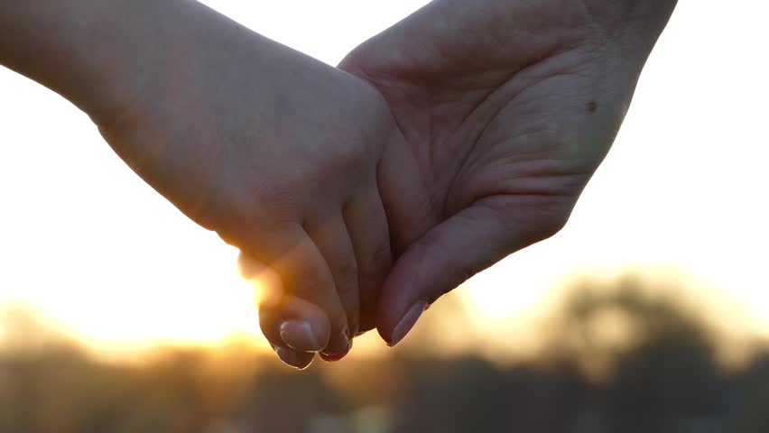 Close the hands of mother and child. Hold hands at sunset. Give a hand to a friend. The sun's rays shine through their fingers. Love, Happiness and Friendship. Hands close up.