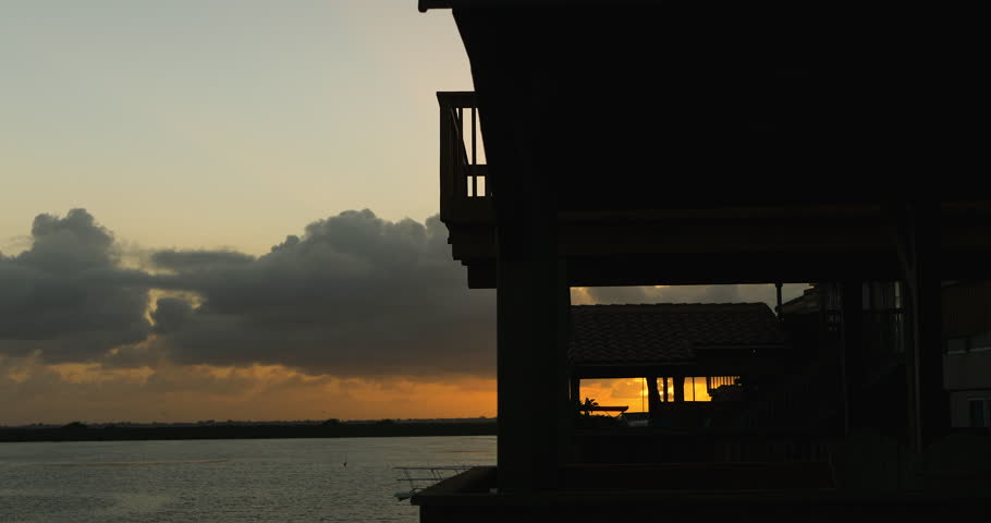 Sunset off the Texas coast behind silhouetted houses and trees.