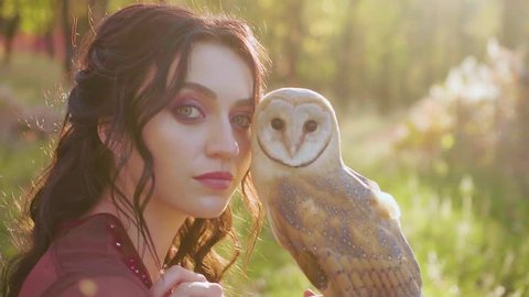 close up Fantasy girl princess. portrait video shooting woman witch with white bird barn owl. Medieval lady queen in red vintage dress. Summer nature forest green grass leaves tree, sunset sun light