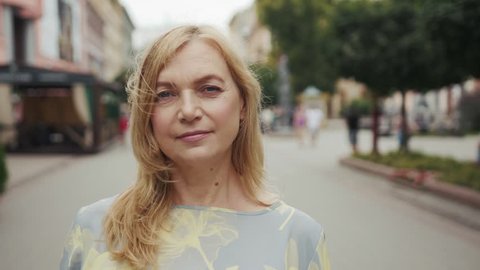 Attractive middle aged blond woman looking into camera stand city center smile portrait senior close up beautiful front outside people person slow motion