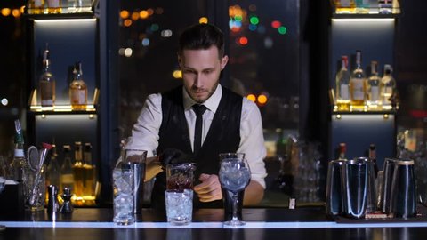 Professional bartender prepared Negroni cocktail and pouring it to oldfashioned glass at bar of modern nightclub. Barman working at bar counter