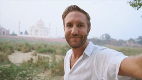 Tourist male taking selfie at the famous Taj Mahal at sunset using mobile phone, Agra, India. People travel Asia concept - Young man travels India and go sightseeing - slow motion
