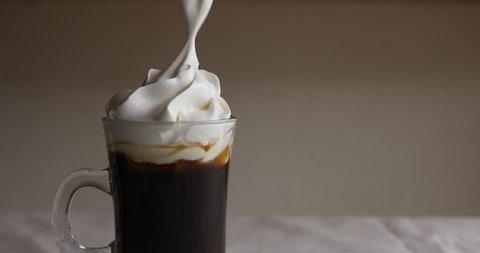Putting whipping cream into glass cup with espresso coffee