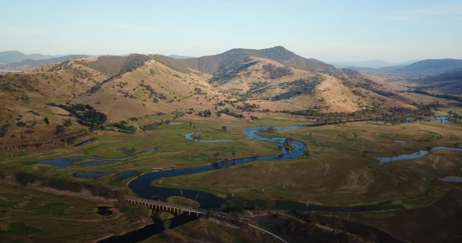 Aerial of river in Outback Australia, summer, magic hour, blue sky reflected in large river at foot of beautiful mountains.