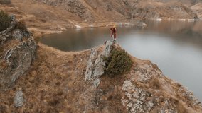 Aerial view of a girl standing on a rock on the shore of a lake, who photographs the landscape on her DSLR camera. Travel videos