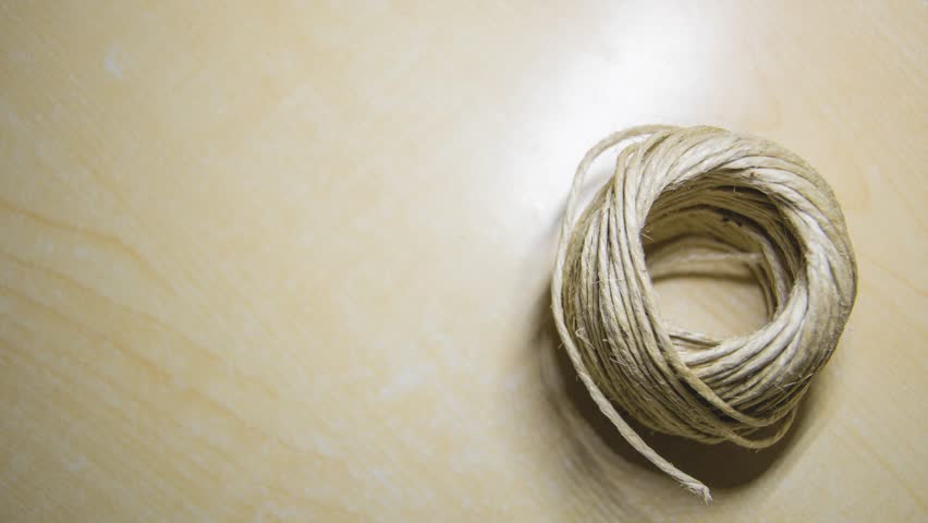 Stop motion of a ball of string unrolling untill it end, on a light wooden background