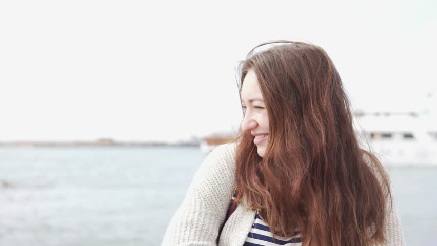 Beautiful woman looks at the sea. Close-up. She is wrapped in a warm wool sweater, her hair flying away from the wind. Winter in Cyprus