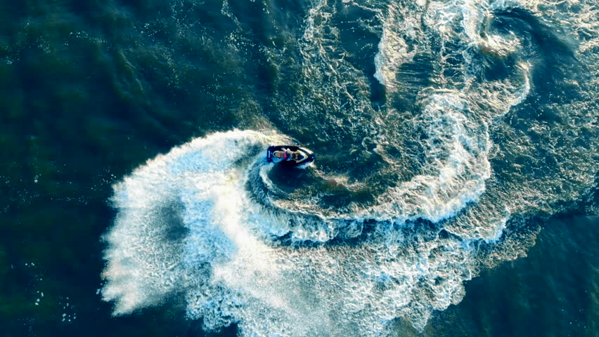 Jetskier is turning on his jet boat, waverunner across the water in a top view.
