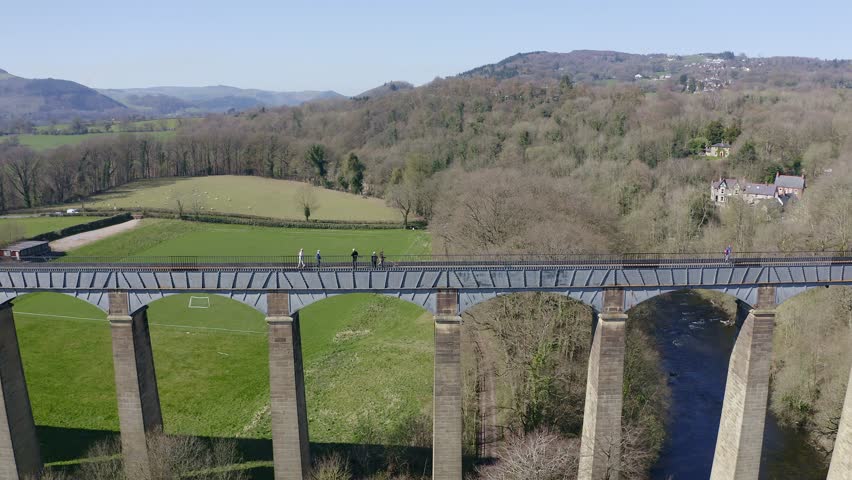 People walk across the beautiful  Narrow Boat canal route called the Pontcysyllte Aqueduct famously designed by Thomas Telford,  located in the beautiful Welsh countryside, A huge bridge viaduct 
