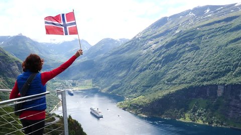 Tourist woman holding norwegian flag, enjoying Geirangerfjord fjord view with large cruise ship. View from Ornesvingen viewpoint. Tourism, travel for relaxation and sightseeing