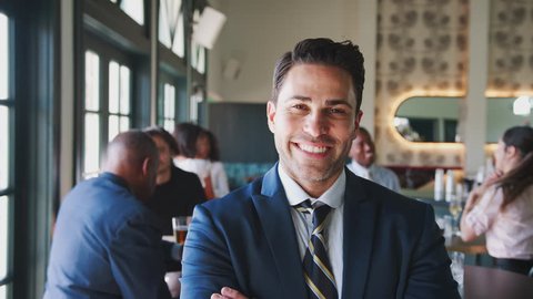 Portrait Of Smiling Businessman In Busy Cocktail Bar Of Restaurant With Customers In Background