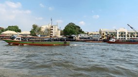 Few multicolored boats are sailing in the sea on the background of the seafront and sunny blue sky with white clouds in Bangkok in Thailand. Video recording with motion to the right.