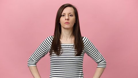 Screaming sad upset young woman in striped shirt looking camera, expressive gesticulating with hands haywire isolated over pastel pink background in studio. People sincere emotions, lifestyle concept.