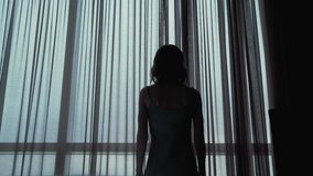 Attractive girl opens the curtains at the window in the hotel