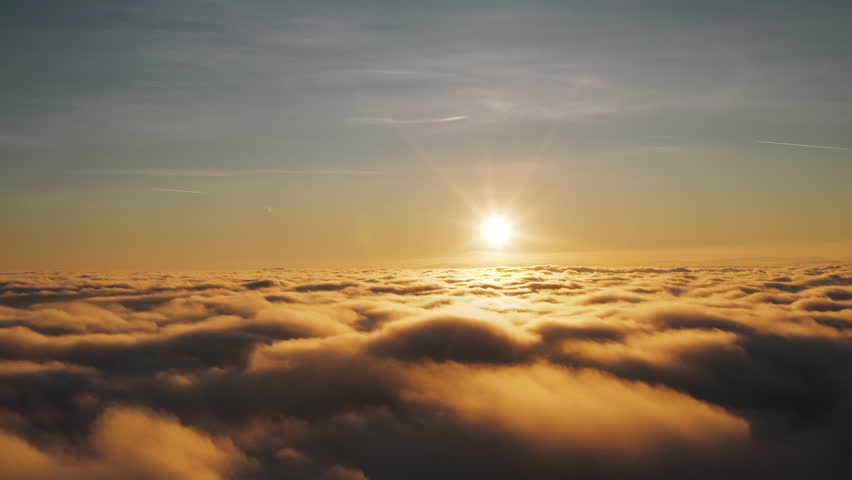 Soaring above fluffy cloud tops that are being illuminated with a orange hue from the sunset.