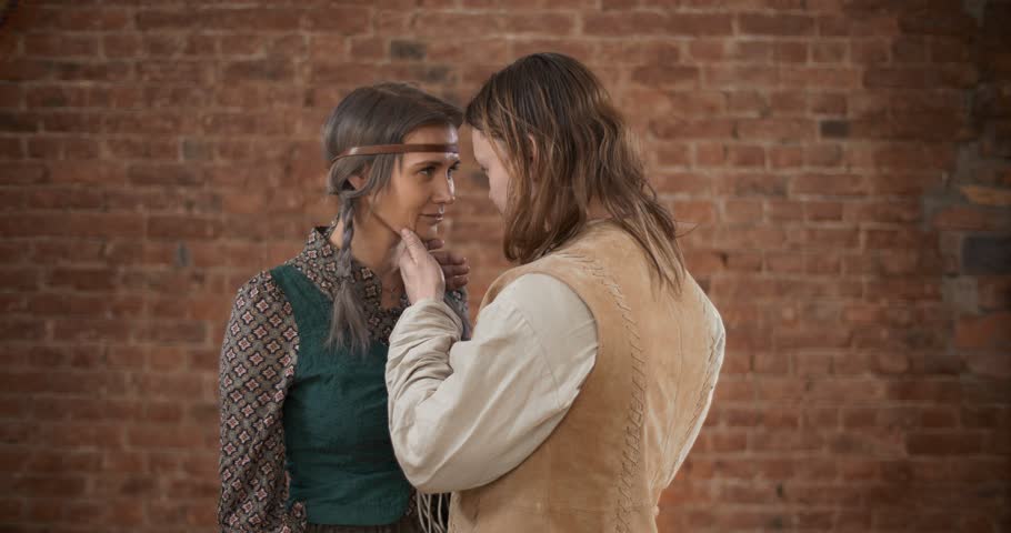 Male farmer in love admiring his lover in barn, touching her face and hugging her. Couple in 19th-century clothes on brick background