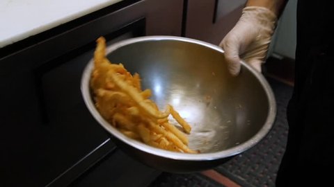 chef flipping flip tosses beer battered fries in metal bowl slow motion.  A chef flips a bowl full of french fries to evenly mix the seasonings.