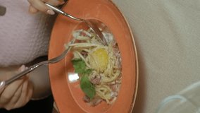 Vertical video. woman in a restaurant eats a hot dish, meat broth with pasta, on the table stands a glass of red wine. Lunch or dinner time. close up hands
