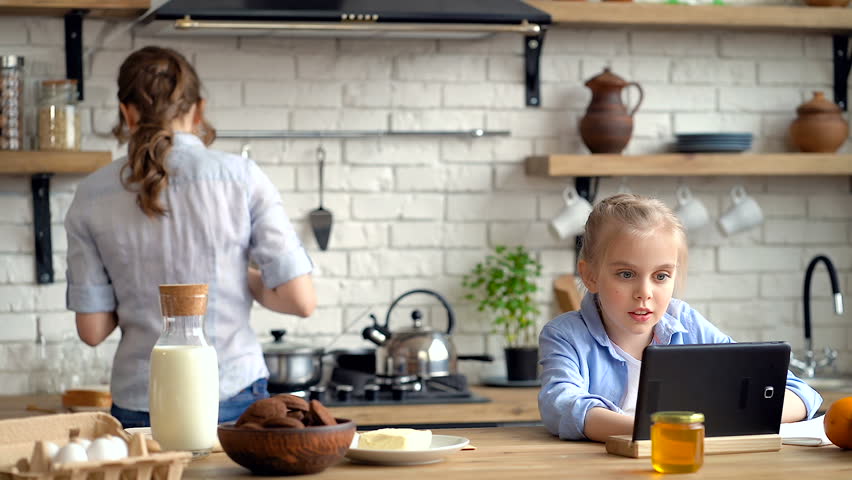 Little girl looking at the tablet. Mother preparing breakfast ang giving butter bread to her. Daughter say thank you mom. Royalty-Free Stock Footage #1026713924