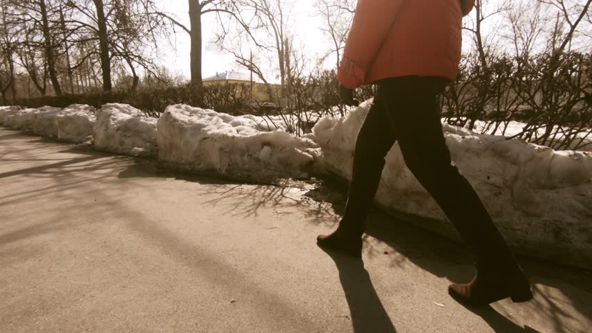 Happy woman in a red jacket walking along the sidewalk in the city. Early spring and puddles. Composition to the waist. The face is not visible.