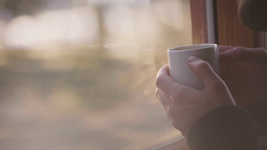 Bearded hipster traveler holding coffee mug in wooden cabin