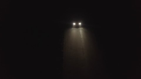 Aerial view tracking a car driving down a rural lane at night at speed.