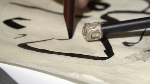 calligrapher writes arabic lettering with calligraphy pen on parchment. macro shot of islamic calligraphy art. close up slider dolly shot in calligrapher workshop table