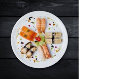 Japanese food. Rotating sashimi set on a white round plate, decorated with small flowers, top view. Black wooden background, square layout for social networks, copy space for your text