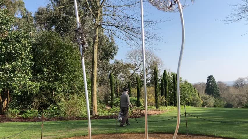 Old charismatic man with walking stick walking in park on a sunny day with blue sky, beautiful view around