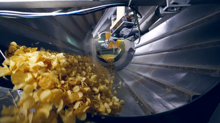 Lots of fried chips sorted in a factory machine, getting mixed with flavor enhancers.